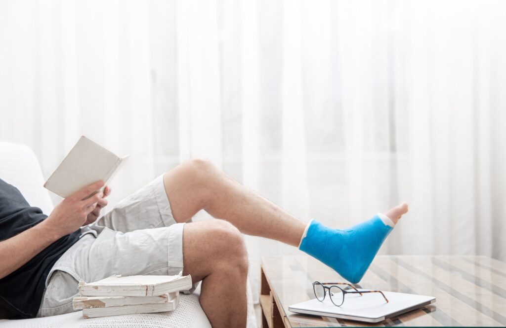 Man with a broken leg in a cast sits at home and reads books.